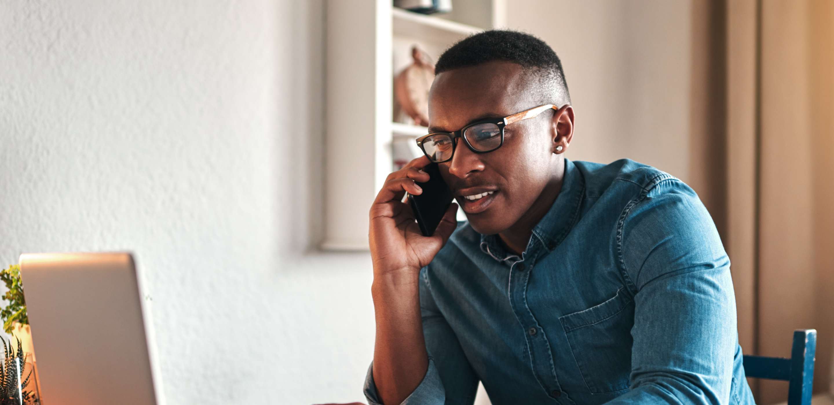handsome young businessman sitting alone in his home office and talking on his cellphone