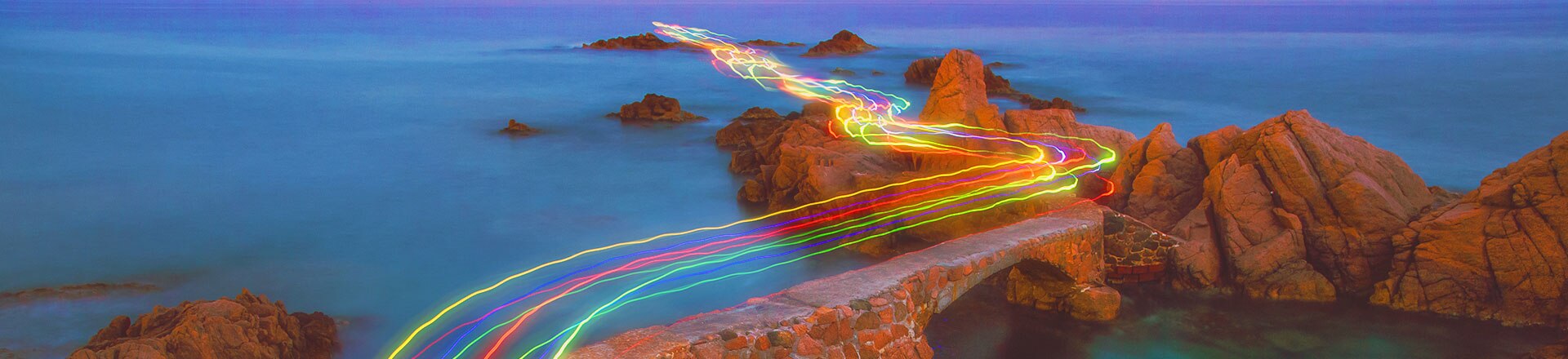 Road with colourful light trails at a body of water