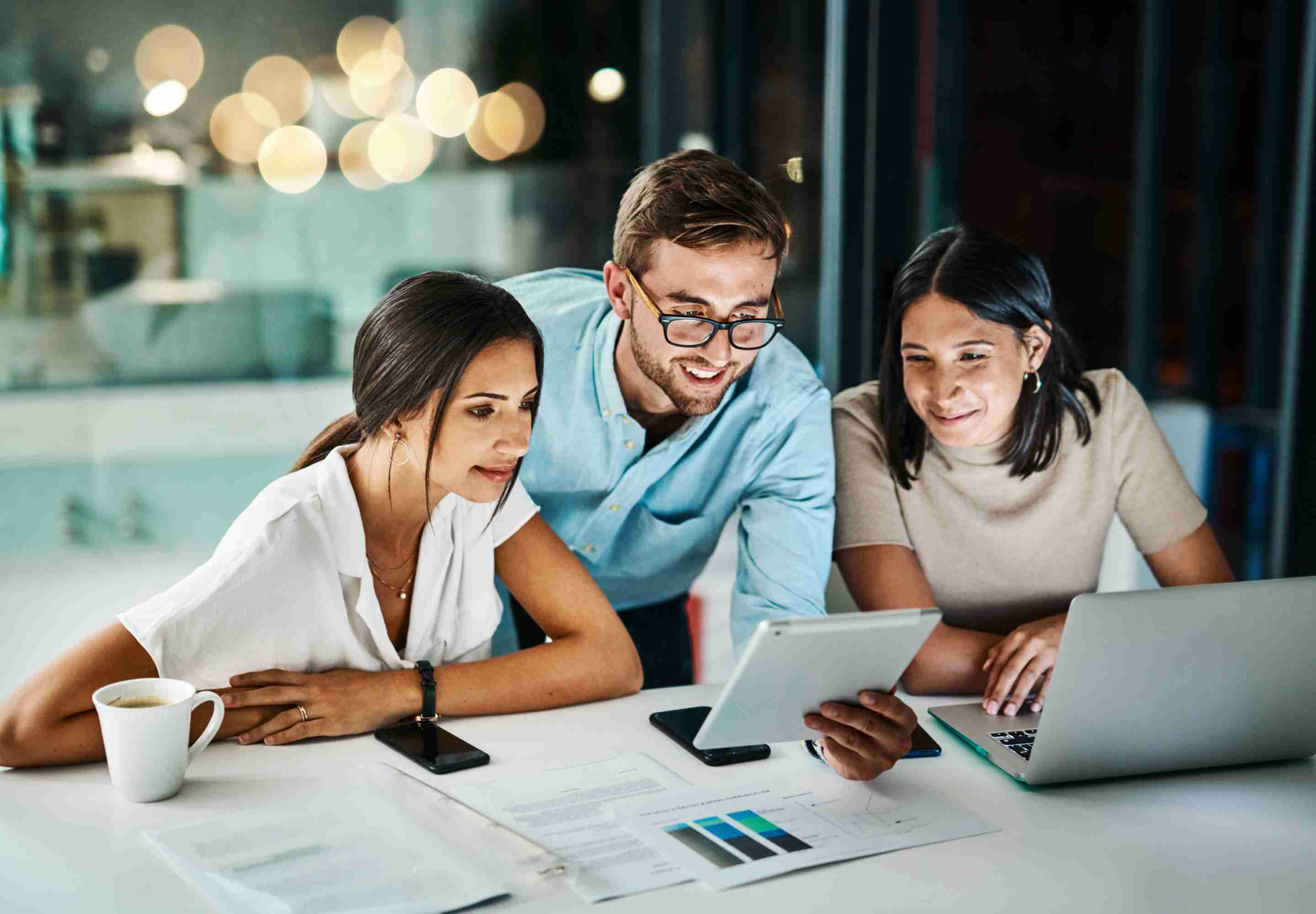 Three people in an office study a tablet. 