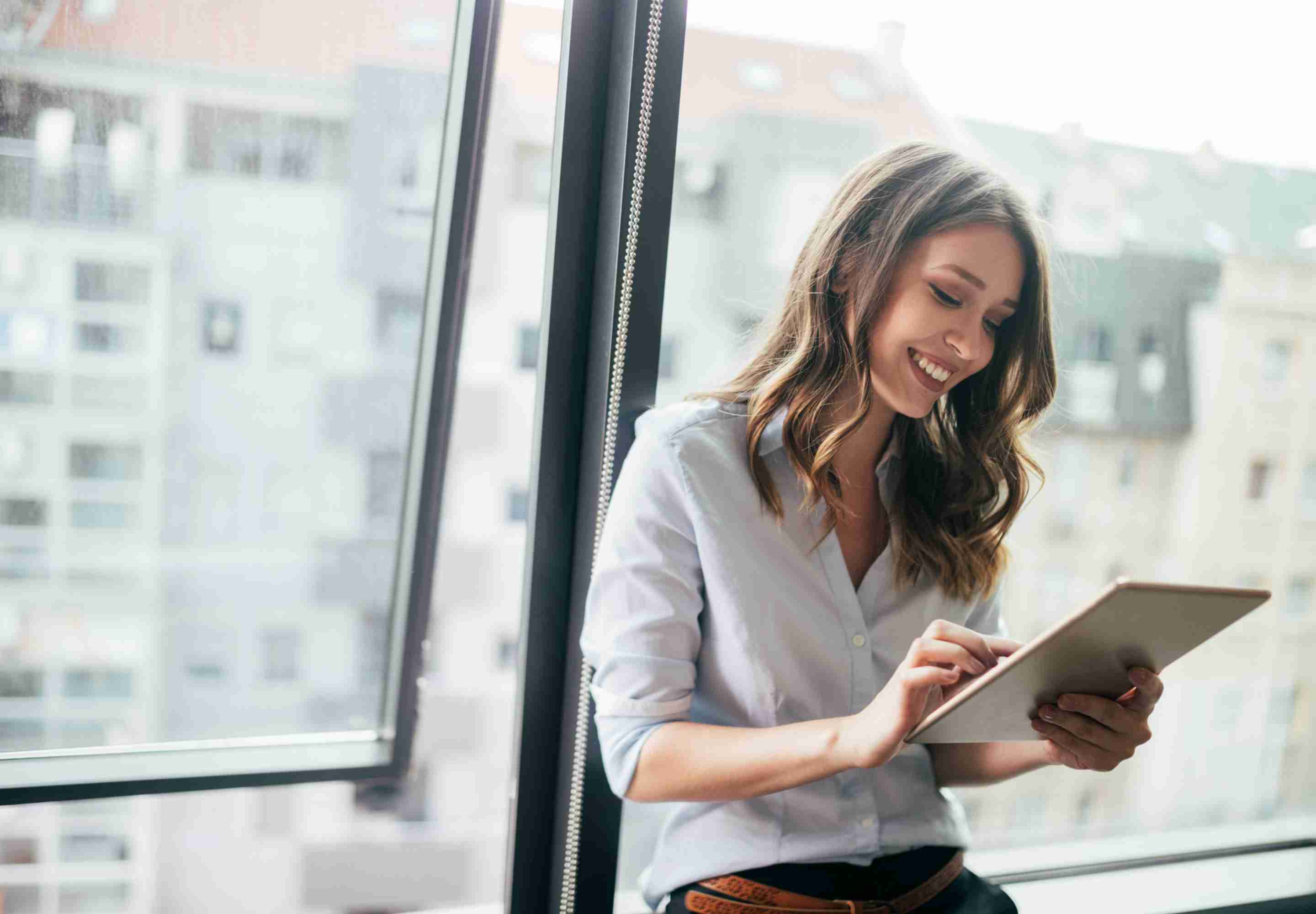 Woman leaning against window looking at tablet