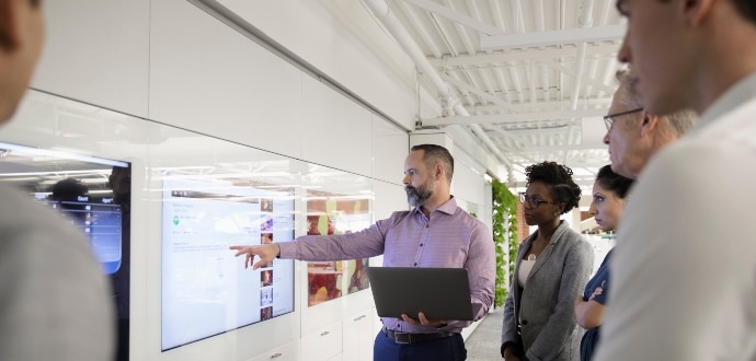 Team standing in a meeting looking at the screen