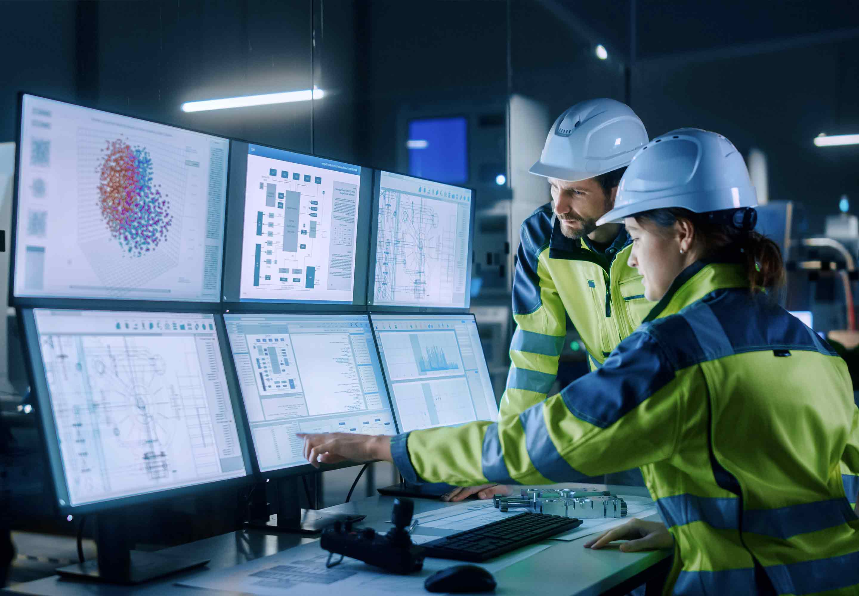 A woman and a man wearing construction gear looking at multiple monitor screens 