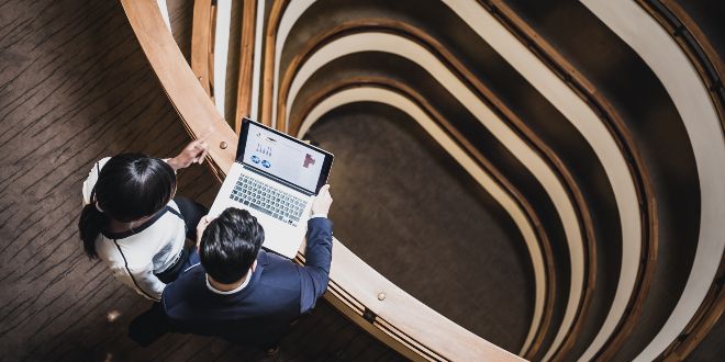 Man and woman standing beside a spiral staircase looking at a laptop